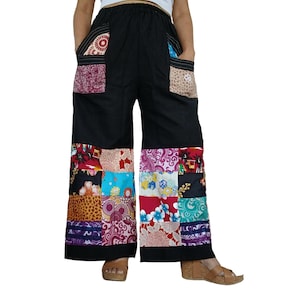 Op de afbeelding: Zwarte broek met wijde pijpen en een patchwork-ontwerp op de onderbenen en zakken. De patchwork-secties bevatten diverse bloemen-, geometrische en dierenprints in tinten rood, blauw, paars, wit en bruin op een zwarte ondergrond.