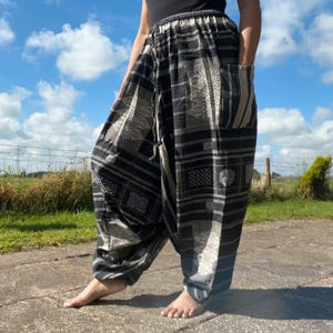 May include: Loose-fitting trousers featuring a black and white geometric pattern with horizontal stripes and intricate square motifs. These wide-leg pants have a high-waisted design with a drawstring closure and deep side pockets on each leg.