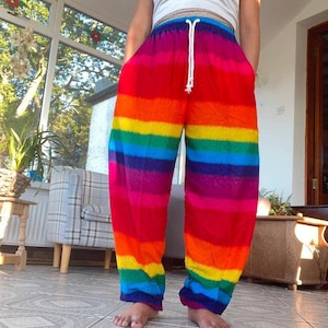 May include: Loose-fitting trousers featuring horizontal stripes in a vibrant rainbow color palette of red, orange, yellow, green, blue, and purple. The pants include an elasticized waistband with a white drawstring cord and side pockets.