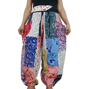 Könnte beinhalten: Patchwork-Hose mit einer Vielzahl bunter Stoffmuster, darunter florale, Paisley- und geometrische Designs. Die Hose hat einen hohen Bund mit weißem Musterbesatz, einen schwarzen Kordelzug und zwei Seitentaschen mit roten Akzenten.