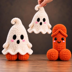 May include: Two cream-colored crocheted ghost figures with black eyes, open mouths, and pink cheeks, one held aloft and one standing on orange crocheted spheres, alongside an orange crocheted phallic figure with black eyes and a smiling mouth.