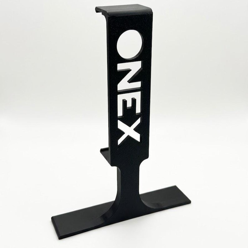 Puede incluir: Un soporte negro vertical en forma de T que presenta una secci&oacute;n vertical rectangular con la palabra ONEX recortada en una fuente sans-serif en negrita. La estructura incluye una base horizontal plana y una peque&ntilde;a secci&oacute;n superior en forma de gancho.