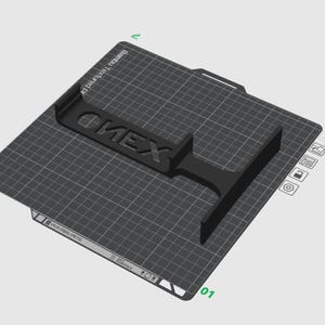 Puede incluir: Un objeto negro impreso en 3D con la palabra ONEX en relieve sobre su superficie, colocado en una placa de construcci&oacute;n cuadrada Bambu Textured PEI. La placa presenta un patr&oacute;n de cuadr&iacute;cula blanca, etiquetas de material y un icono de advertencia.