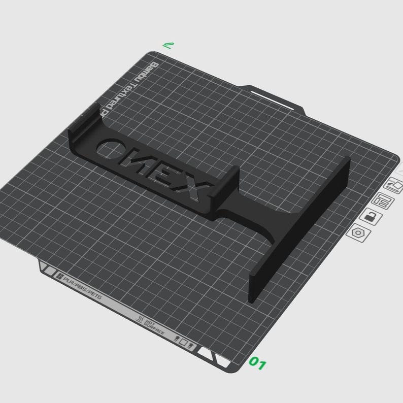Puede incluir: Un objeto negro impreso en 3D con la palabra ONEX en relieve sobre su superficie, colocado en una placa de construcci&oacute;n cuadrada Bambu Textured PEI. La placa presenta un patr&oacute;n de cuadr&iacute;cula blanca, etiquetas de material y un icono de advertencia.
