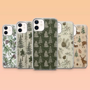 May include: Five clear smartphone cases featuring various winter-themed patterns including pine branches with cones, evergreen tree silhouettes, mistletoe, and a scene with deer, snowflakes, and small cabins on a light background.