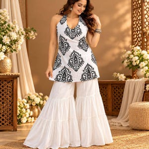 May include: A white halter-neck top featuring a black paisley print paired with matching white wide-leg tiered palazzo pants. The top has a deep V-neckline and a sleeveless design, while the pants have a flowing, layered silhouette.