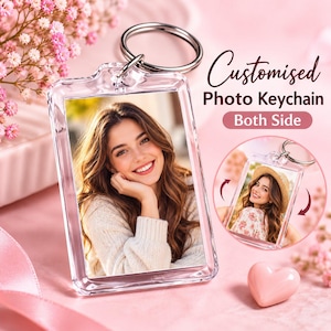 Puede incluir: Un llavero rectangular de acrílico transparente con una anilla metálica. El llavero muestra el retrato de una persona sonriente con el pelo largo y castaño. El texto dice Customised Photo Keychain Both Side. Un recuadro circular muestra el reverso.