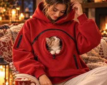 May include: A bright red hooded sweatshirt featuring a large circular front pouch with a black zipper, designed to carry a small cat. The hoodie includes long sleeves with ribbed cuffs, a drawstring hood, and additional zippered pockets.