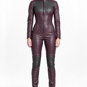 May include: A long-sleeved, full-length jumpsuit crafted from deep burgundy leather. It features a central black zipper, a high collar, and black quilted leather panels on the chest and knees. The garment has a fitted silhouette and long sleeves.