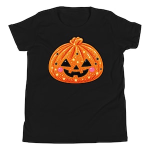 May include: A black short-sleeve t-shirt featuring a central graphic of a glittery orange pumpkin with a smiling jack-o'-lantern face. The pumpkin design includes small black and yellow star accents and two pink circular cheeks on a dark background.