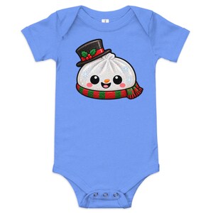 May include: A light blue short-sleeve baby bodysuit featuring a graphic of a white dumpling character wearing a black top hat with holly berries, a red and green striped scarf, and small blue snowflakes on its round body.