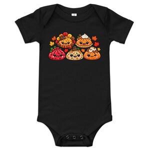 May include: A black short-sleeved baby bodysuit featuring a central graphic of five anthropomorphic Thanksgiving-themed food items, including pies and stuffed pastries with smiling faces, surrounded by small orange, red, and yellow autumn leaves.