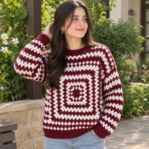 May include: A long-sleeved sweater featuring a crochet granny square pattern in alternating stripes of deep burgundy and off-white. The garment has a round neckline and ribbed cuffs and hem, constructed with a textured, open-stitch yarn design.