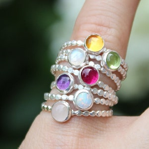 May include: A stack of silver rings with colorful gemstones, including pink, red, white, green, and yellow.