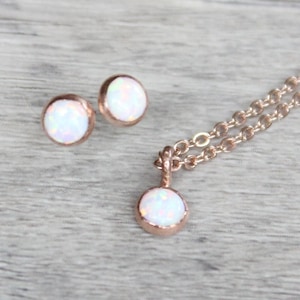 May include: A set of rose gold jewelry featuring a necklace and earrings with white opal stones.