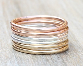 Pode incluir: Uma pilha de anéis finos de ouro, prata e ouro rosa. Os anéis estão empilhados uns sobre os outros, criando um visual em camadas.
