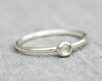 May include: A simple silver ring with a small, round, white gemstone.