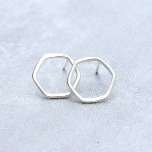 May include: A pair of silver hexagon shaped earrings. The earrings are simple and modern.