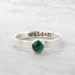 May include: A silver ring with a green gemstone and the word "walden" engraved on the band.