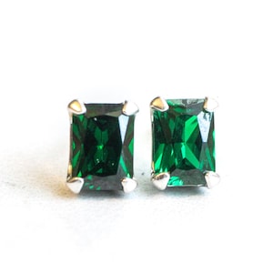 May include: A pair of emerald green square-shaped stud earrings with silver settings.