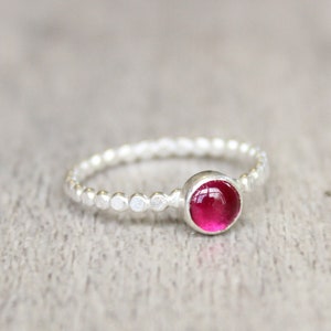 May include: A silver ring with a textured band and a round, bright pink gemstone.