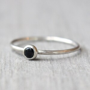 May include: A simple silver band ring with a small black gemstone set in the centre.