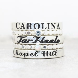 May include: Stack of five silver rings with engraved text. The top ring says "CAROLINA", the second ring says "Tar Heels", and the bottom ring says "Chapel Hill".