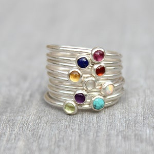 May include: A set of seven silver rings with colorful gemstones. The rings are stacked on top of each other, and the gemstones are visible. The gemstones are a variety of colors, including red, orange, yellow, green, blue, purple, and white.