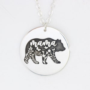 May include: Silver necklace with a round pendant featuring a black bear silhouette with floral details and the word "mama" inscribed inside.