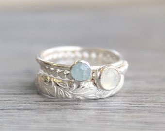 Könnte beinhalten: Ein silberner Ring mit drei Steinen. Die untere Band ist mit einem Blattdesign strukturiert. Die mittlere Band ist eine einfache silberne Band mit kleinen Perlen. Die obere Band hat einen hellblauen Stein und einen weißen Stein.