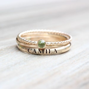 May include: A set of three gold rings with a green gemstone. The bottom ring is engraved with the name "CAMILLA".