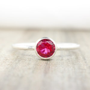 May include: A silver ring with a bezel setting featuring a bright red ruby gemstone.