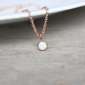 May include: A delicate rose gold necklace with a small, round white opal pendant.