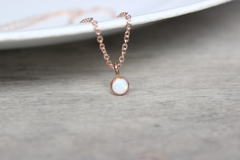 May include: A delicate rose gold necklace with a small, round white opal pendant.