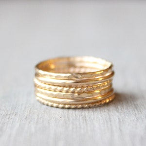 May include: A set of seven gold stacking rings, featuring a variety of textures, including hammered, twisted, and smooth finishes.