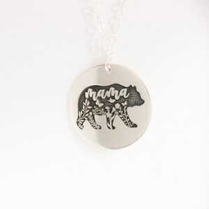 May include: Silver necklace with a round pendant featuring a bear silhouette with floral details and the word "mama" inscribed inside.