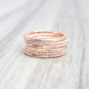 May include: Set of five rose gold stacking rings. The rings are different widths and have a hammered and rope-like texture.