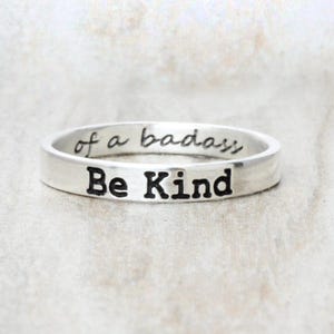 May include: A silver ring with the words "Be Kind" engraved on the front and "of a badass" engraved on the inside.