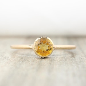 Puede incluir: Un anillo de oro con una piedra preciosa redonda de citrino amarillo. La piedra preciosa tiene un patrón en forma de estrella.