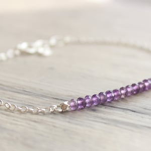 May include: A delicate silver chain bracelet with a row of small, purple amethyst beads.
