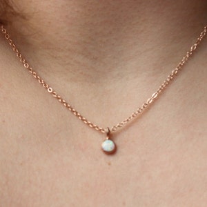 May include: A delicate rose gold chain necklace with a small white opal pendant.
