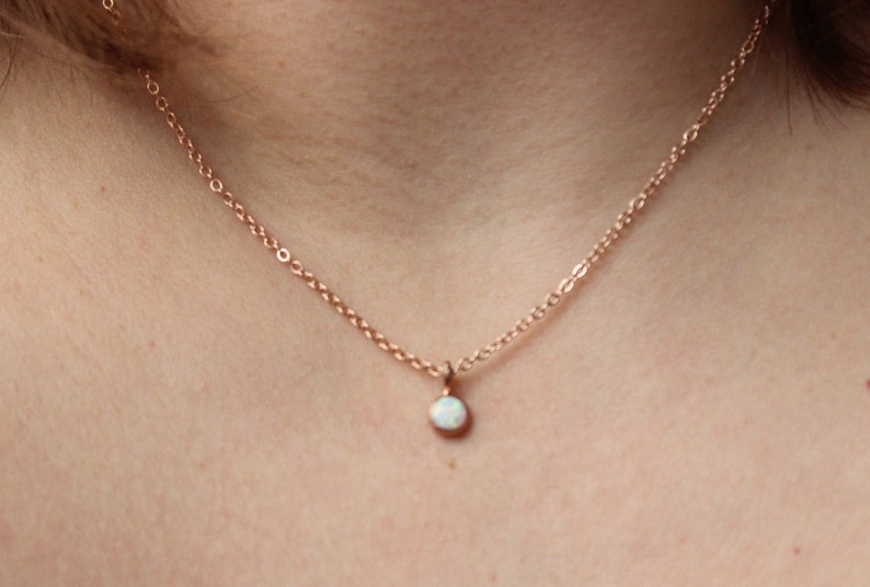 May include: A delicate rose gold chain necklace with a small white opal pendant.