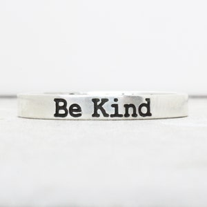 Puede incluir: Un anillo de plata con las palabras "Be Kind" grabadas.