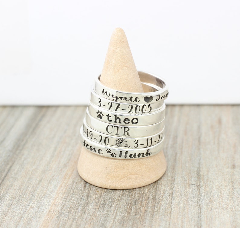 May include: Stack of silver rings with engraved names and dates, including "Wyatt 3-27-2005", "theo", "CTR", "Jesse", and "Hank".