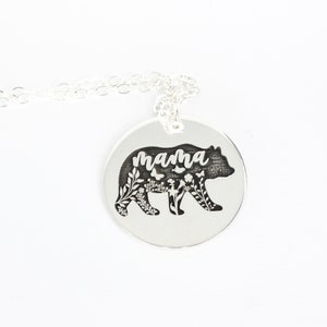 May include: Silver necklace with a round pendant featuring a bear silhouette with floral details and the word "mama" inscribed.