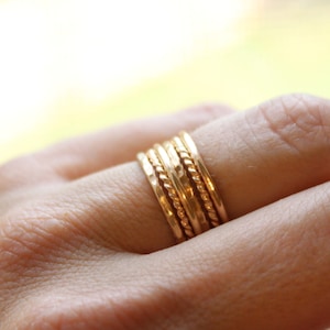 May include: A set of five gold stacking rings with different textures, including a rope design, a hammered finish, and a smooth band.
