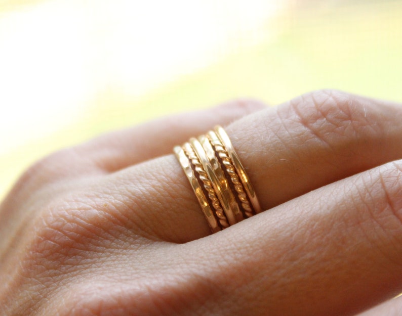 May include: A set of five gold stacking rings with different textures, including a rope design, a hammered finish, and a smooth band.