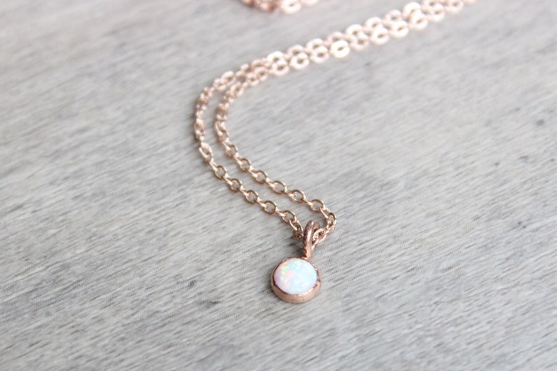 May include: A delicate rose gold necklace with a small white opal pendant.
