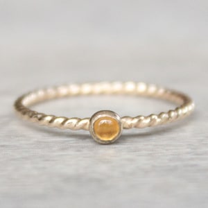 May include: A delicate gold ring with a twisted band and a small, round, orange gemstone.