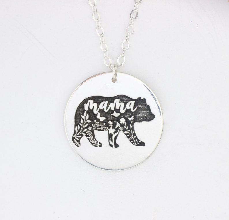 May include: Silver necklace with a round pendant featuring a black bear silhouette with floral details and the word "mama" inscribed inside.